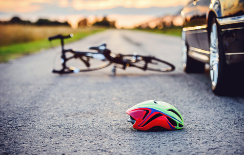 Bicycle helmet on the road with a bicycle and vehicle in the background after a crash