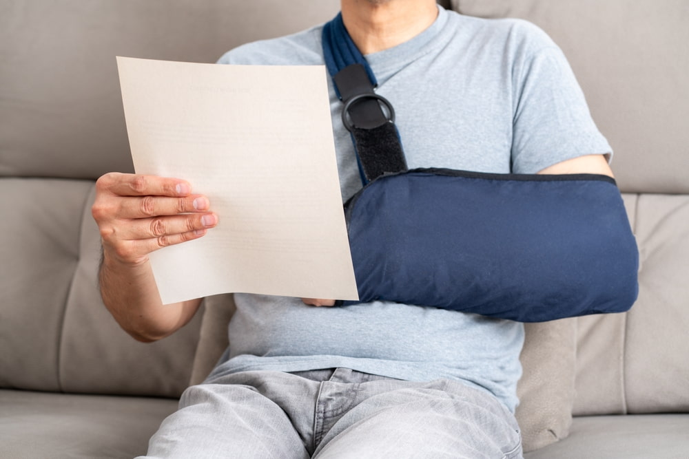 Person wearing an arm sling while reading a document on a couch