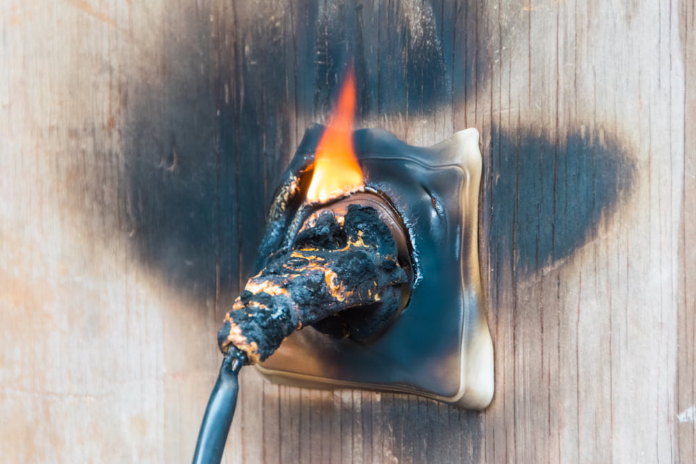 Electrical plug and wall outlet melting and burning against a scorched wooden wall