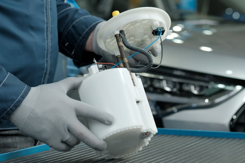Technician wearing gloves and inspecting an automotive fuel pump assembly beside a vehicle
